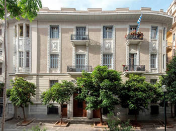 A beige, three-story building with trees on the sidewalk
